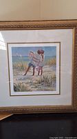 Framed color lithograph showing two children playing on the beach with detailed coastal scenery