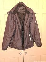 Dark grey men's coat hanging on door, front view showing zipper and sleeves