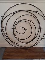 Photo showing the large spiral metal candle holder resting on the floor against a wall with a wooden base and multiple metal arms for candles