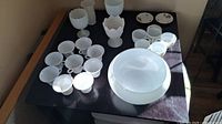 View showing entire lot of white punch bowl and two sets of cups on black table.