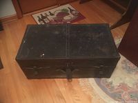 Closed black metal antique trunk on wooden floor with visible wear and scratches.