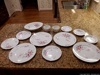 Full set of 13 pieces of Harmony House Dogwood china arranged on counter including plates, cups, saucers, and oval bowl.