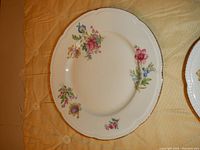 Floral pattern scalloped small plate with pink, purple, blue flowers and gold trim on a quilted background