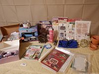 Photo showing the full assortment of craft items including boxed paint set, instructional books, jars, pots, and tools arranged on a beige surface.