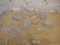 Overview of all 15 crystal pieces arranged on a tablecloth, showing variety in shapes and sizes including bowls, vase, and rectangular dish.