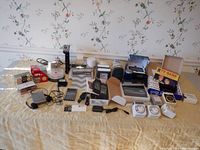 Wide layout of all household electronics items spread on a table showing timers, calculators, phones, media items, and chargers.