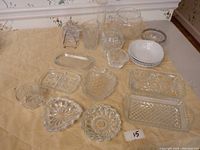 Full overview of kitchen glassware laid on a beige cloth, showing bowls, serving dishes, ashtrays, coasters, and shaped glassware