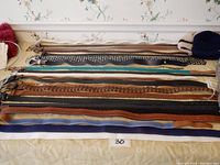 Photo showing laid out belts of various styles and colors, plus partial view of hats and gloves on edges.