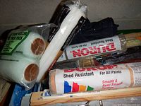 Shelves containing various paint supplies including new paint rollers with foam covers, roller handles, and sanding materials.