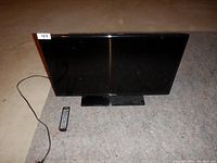 Samsung 32 inch LED-LCD HDTV with its stand and power cable on carpeted floor, accompanied by a remote control.