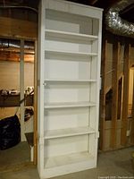 Front view of tall white wood shelving unit with 6 shelves used in workshop environment
