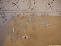 Photo showing 31 various specialty drinking glasses arranged on a table including many clear crystal glasses with different stem lengths and bowl shapes.