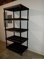 Full view of 5-tier black plastic shelving unit showing length, width, and height with a dolly cart beneath (not included). The shelves have slatted construction.