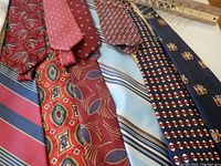 View of various men's ties laid out showing multiple colors and patterns including stripes, geometric, and floral designs along with the wooden and gold-tone horizontal tie rack.