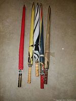 Five golf umbrellas with wooden handles in various colors and covers laid out on ground