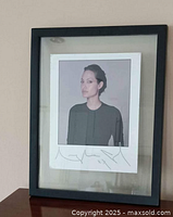 Framed signed photo of Angelina Jolie against beige wall, showing large signature beneath the image.
