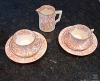 Two sets of teacups with matching saucers and side plates arranged with a creamer, showing the red coral seaweed pattern on porcelain.