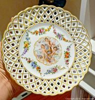 Full view of hand holding the vintage Von Schierholz Dresden porcelain plate showing reticulated gold trimmed border with floral and cherub design.