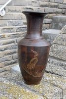 Photo of the brown ceramic vase showing the tall narrow neck and carved crane design outdoors against stone steps.