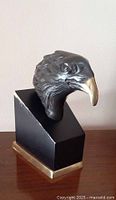 Front angled view of vintage cold cast bronze eagle head bust on black wooden base with brass trim.