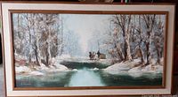 Framed oil painting featuring a winter landscape with snow-covered trees and a green river or stream in the foreground, horse-drawn sleigh in background.