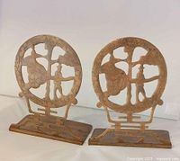 Pair of antique/vintage Chinese brass bookends showing circular dragon design with human figure, with oxidation and patina on brass surface, photographed against white background under good lighting.