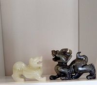 White and green jade foo dog figures side by side on shelf against white background.