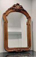 Full view of classical carved wood framed wall hanging mirror, showing the ornate carved top and bottom details of the wood frame and reflective mirror surface.