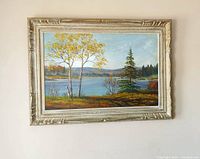 Framed landscape oil painting by Edgar Marlow hanging on a wall, showing lake, trees, and distant hills in autumn colors.