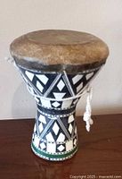 Side view of the small Egyptian drum showing circular natural leather drumhead and black and white geometric wood inlay on the tapered wooden body, with white rope tied for tension.