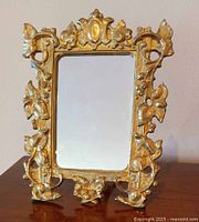Front view of antique French gilded bronze vanity table mirror showing detailed floral and leaf motifs on frame.