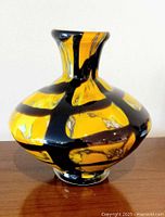 Front view of vase on tabletop showing orange ground and black overlay pattern