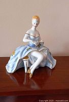 Front angle photo showing the lady figurine in a blue detailed dress with raised fan and seated pose.