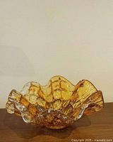 View of amber Murano glass bowl showing organic wavy rim and square textured pattern inside.