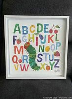 Framed colorful alphabet print showing The Very Hungry Caterpillar character with letters and fruits on a white background.