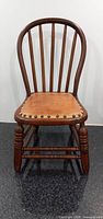 Front view of the vintage Windsor children's chair showing its curved back and leather seat with decorative nails