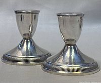 Two polished vintage sterling silver weighted candle holders side by side on a neutral surface.