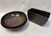 Photo showing 3 round bakelite bowls with mottled green and red marbled finish stacked and 3 dark brown rectangular bakelite planters with footed base stacked next to them.