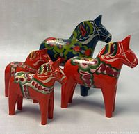 Four hand-painted wooden Dala horses standing in a group showing their colorful folk art designs, three red and one blue horse.