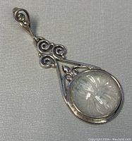 Front view of the silver pendant showcasing the carved moonstone and scrollwork.