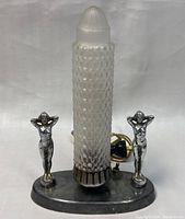 Front view of the Art Deco lamp showing the frosted glass shade and two silver plated female figurines on metal base with electrical cord and switch.