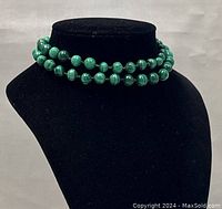 Necklace displayed coiled on black velvet bust showing color and bead details.