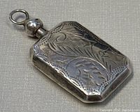 Close-up photo of the rectangular silver perfume bottle pendant showing intricate floral engraving and spherical silver cap with loop.