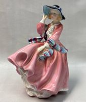 Front view of Royal Doulton figurine showing the woman in a flowing pink dress with blue and white accents, holding her hat.