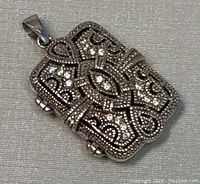 Close-up of intricately hand decorated front of the vintage silver locket pendant showing detailed patterns and clear stones.