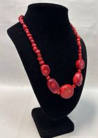 Necklace draped on black bust showing overall design, bead shapes and vibrant red color