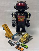 Front view of Robotron RT-2 robot toy with five diecast vehicles in front including yellow crane, forklift, and small cars