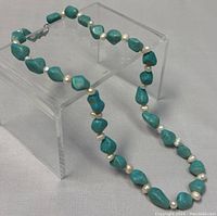 Full view of the turquoise and freshwater pearl necklace on a clear stand.