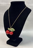 Necklace displayed on a black bust showing full length chain and cherry pendant with red cherries and green rhinestone leaves.