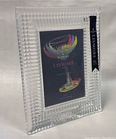 Front angle photo of Waterford Lismore crystal photo frame with label and colorful illustrative card inside.